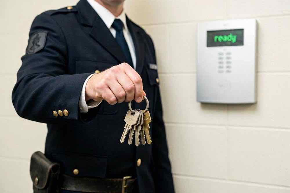 Security officer holding keys beside an alarm panel, Belfast